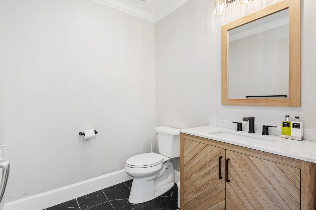 White bathroom with wall-mounted toilet and wooden vanity - bathroom remodeling services Long Beach NY